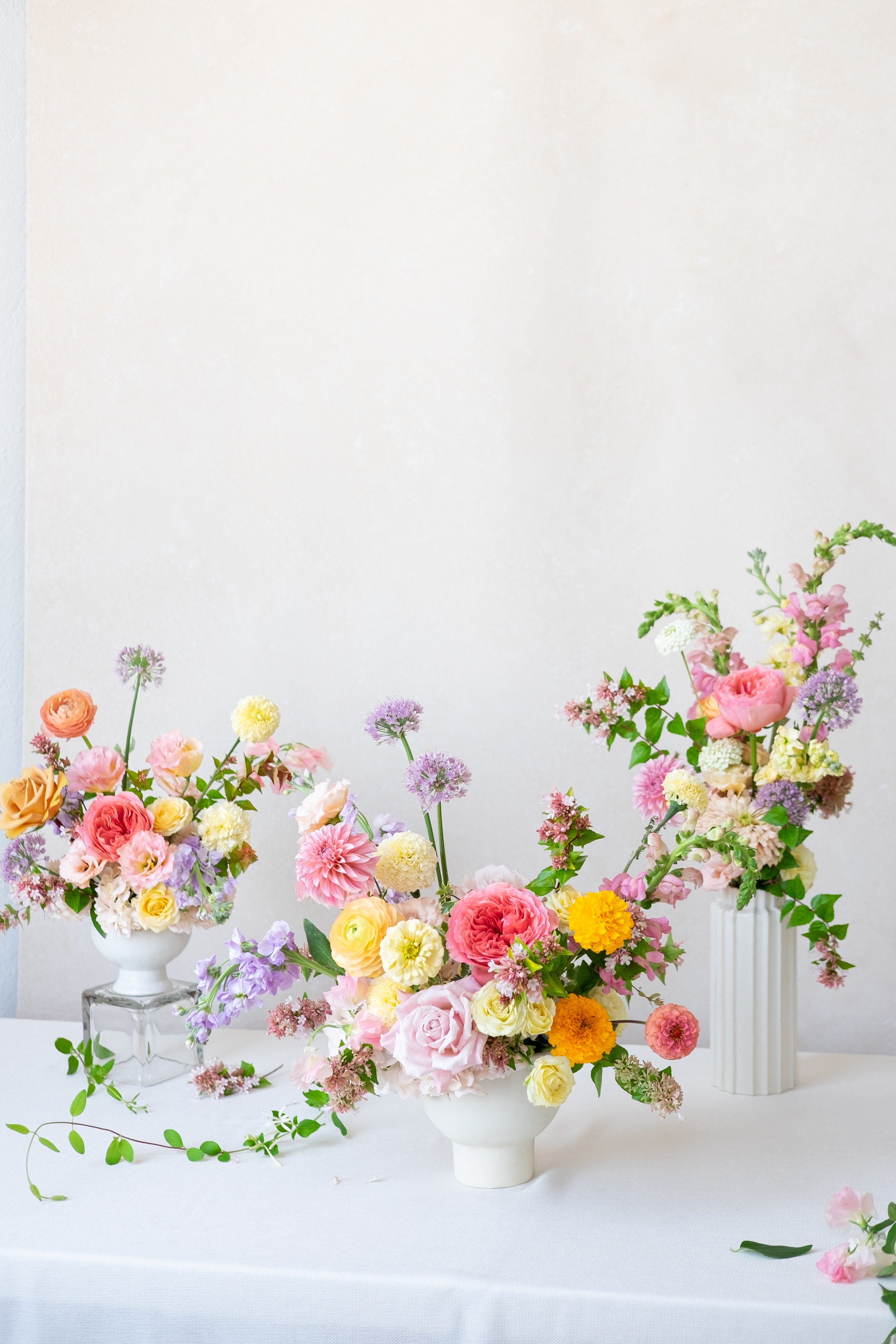 Colorful floral arrangements in white vases on a white tablecloth with a white background