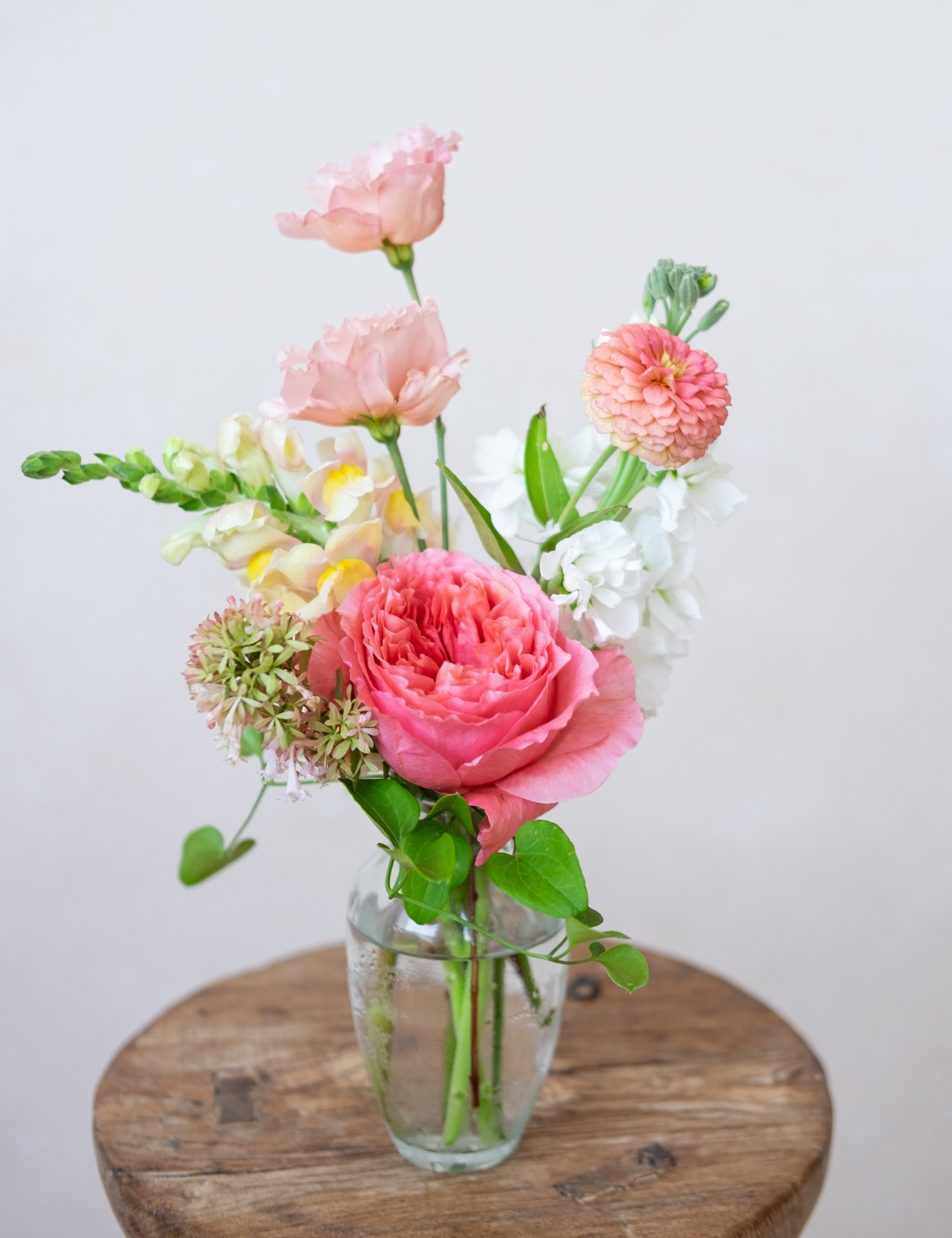 Vase of pink and white flowers on a wooden surface with a light background