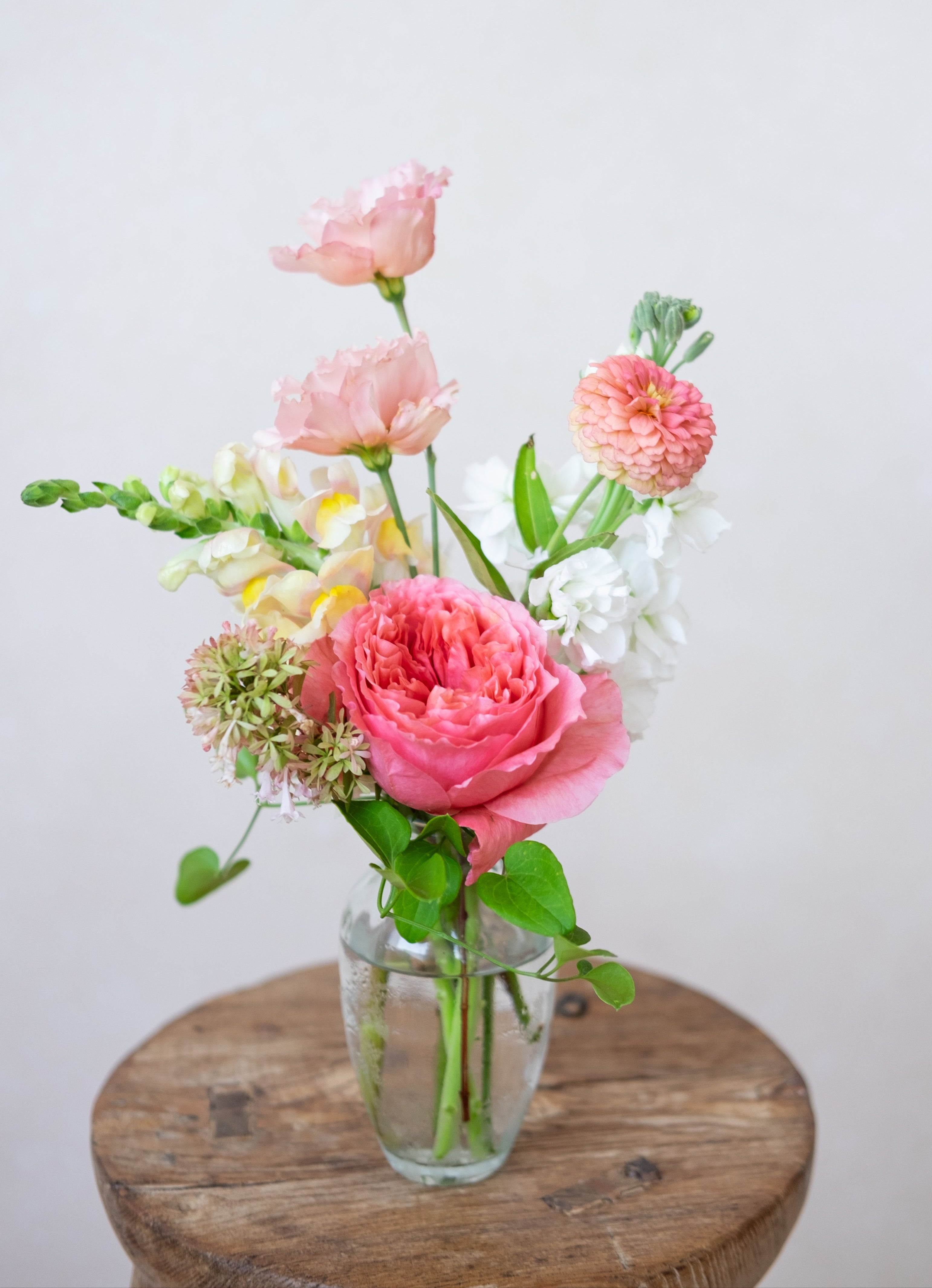 Vase of pink and white flowers on a wooden surface with a light background