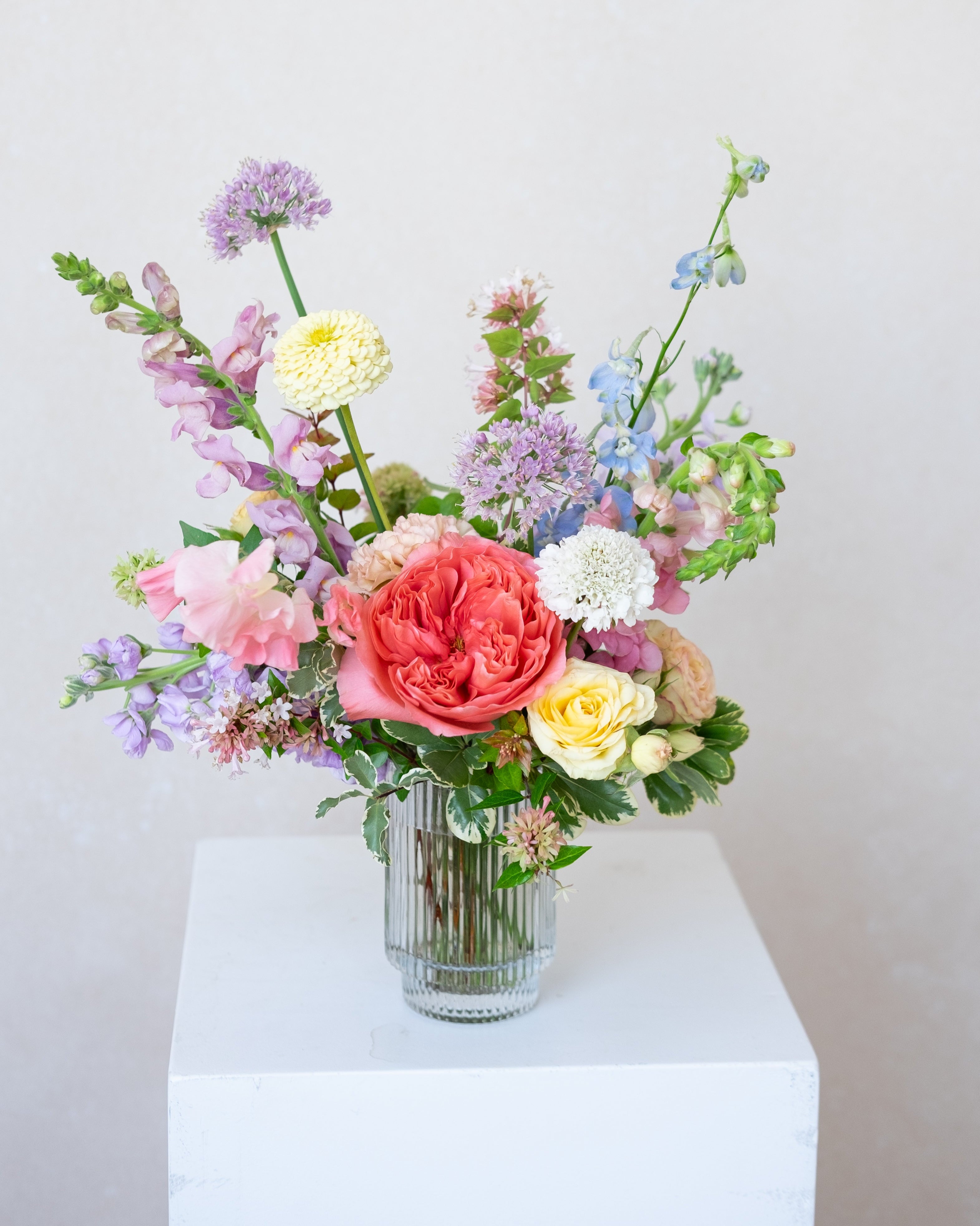 Colorful flower arrangement in a glass vase on a white surface with a light gray background