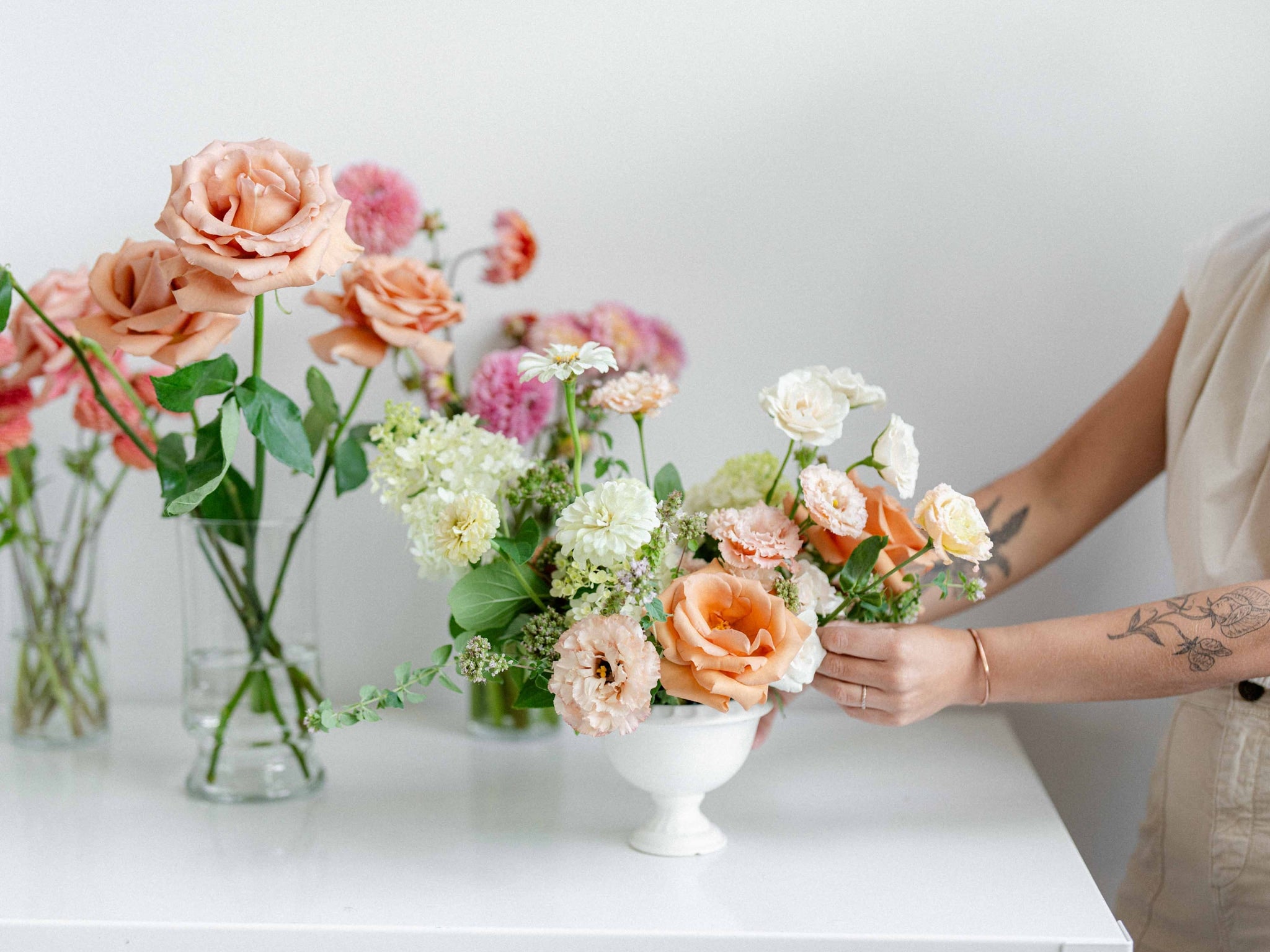 Person arranging flowers on a white table with a neutral background