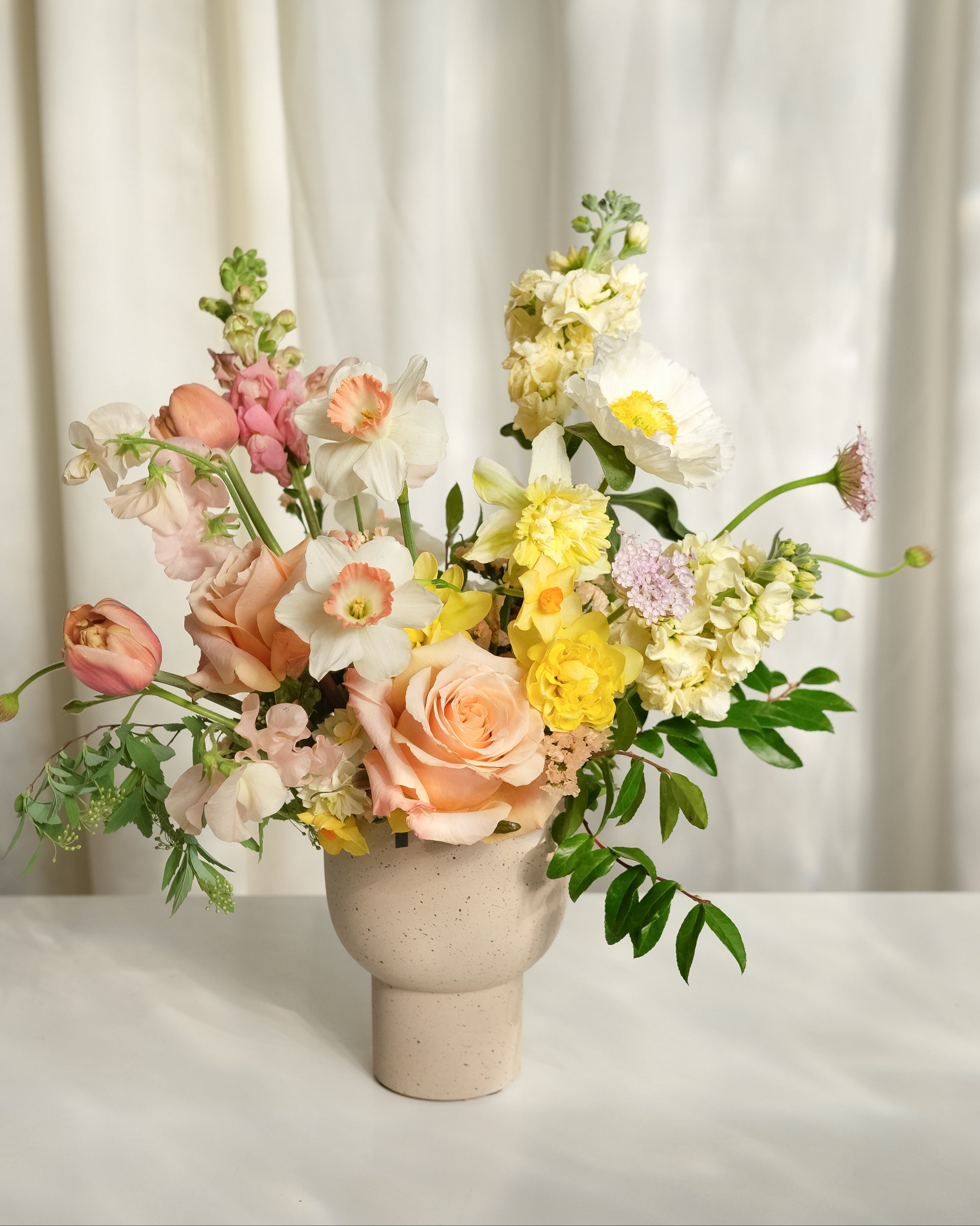 Floral arrangement in a vase on a white surface with a light curtain background