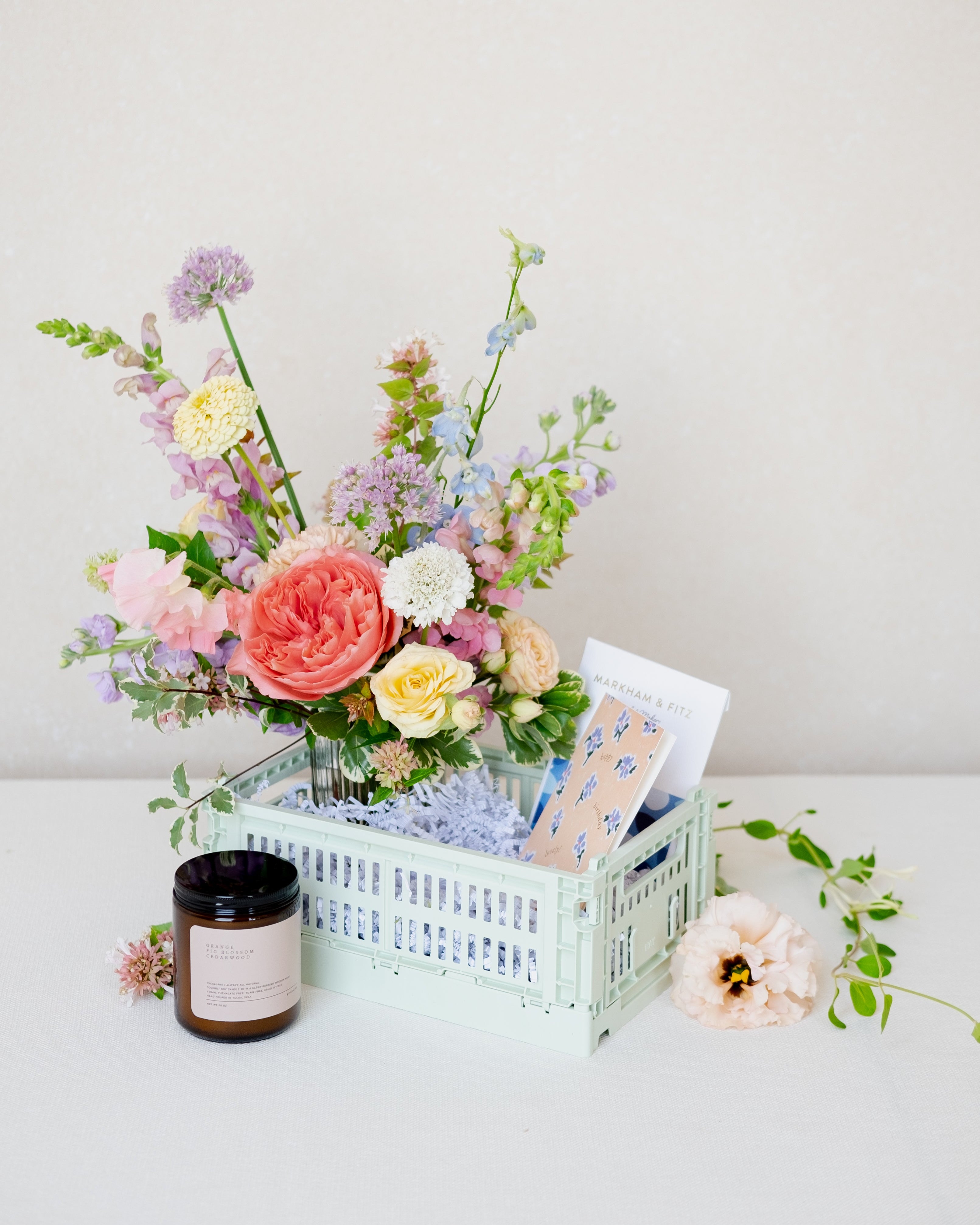 Floral arrangement in a crate with a candle on a white surface