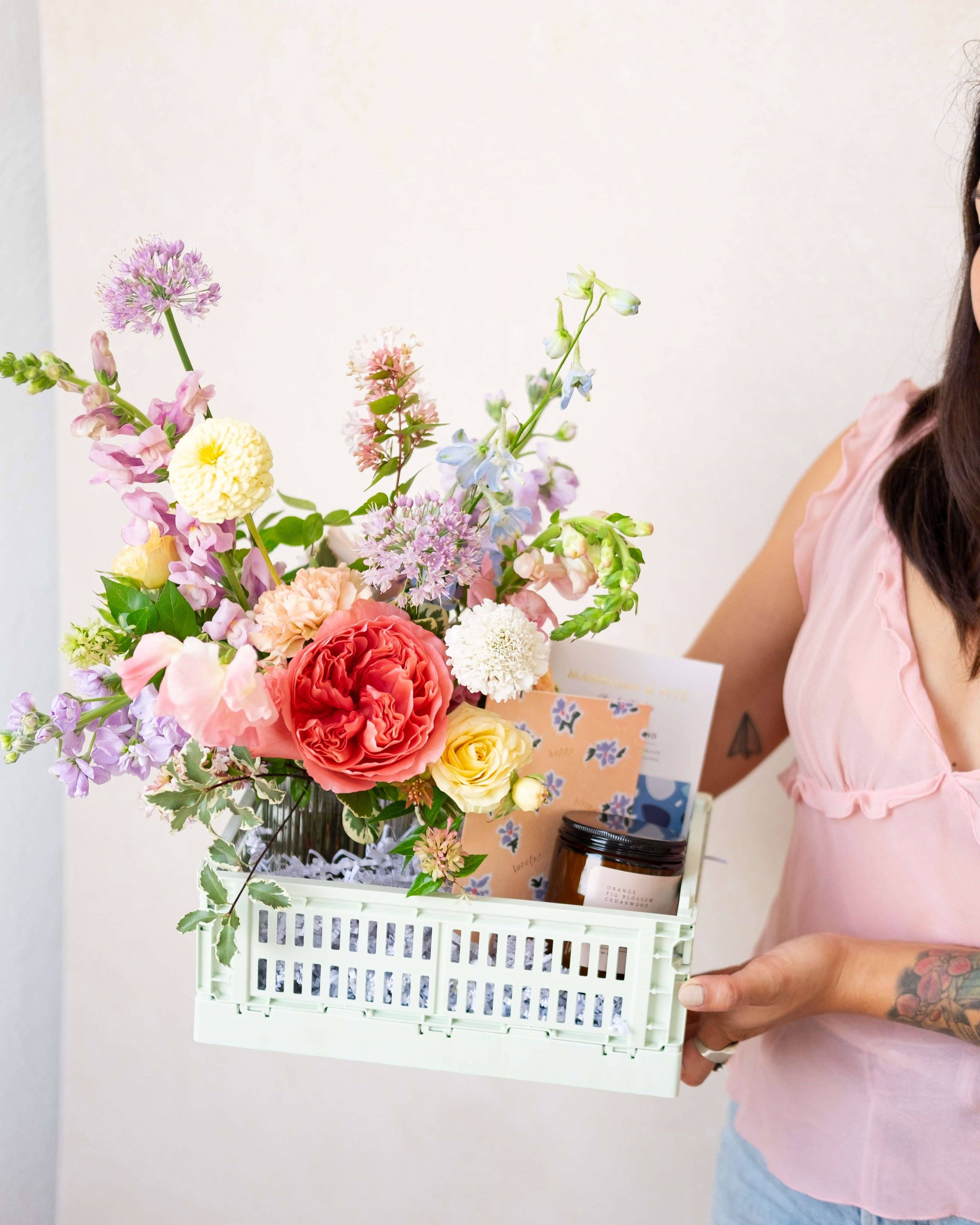 Person holding a colorful bouquet of flowers and a box against a white background