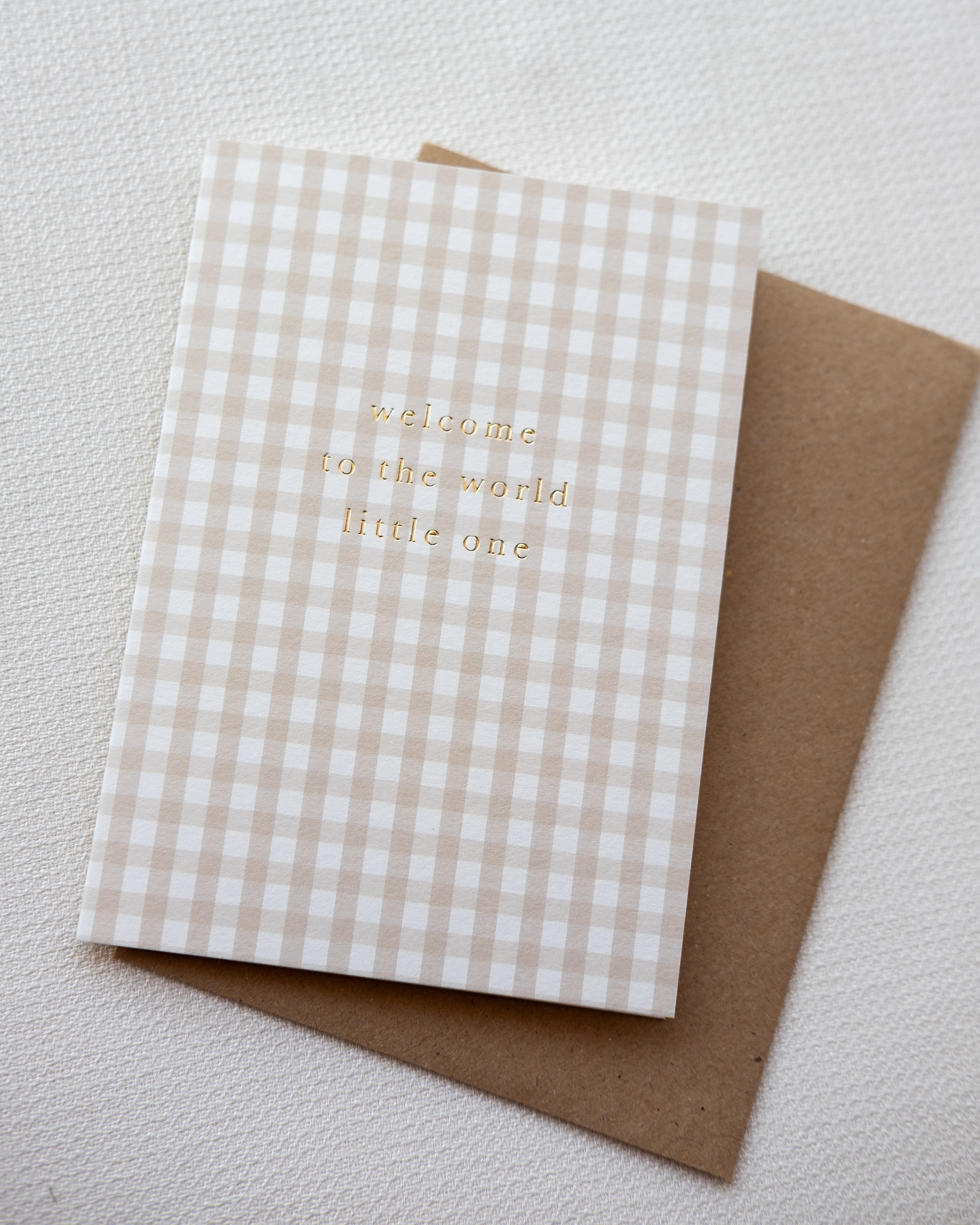 Checkered card with 'welcome to the world little one' text on a textured surface